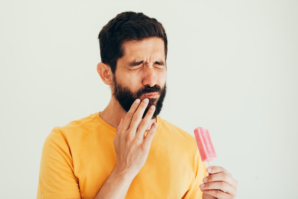 man with popsicle wincing in pain