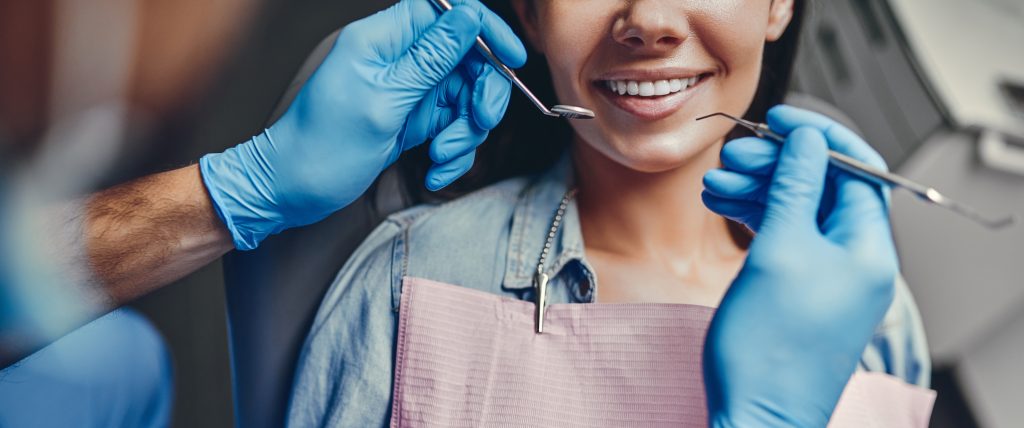 Young adult woman smiling while a dentist examines her mouth with dental tools