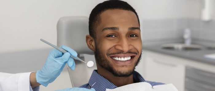 African american man smiling and sitting in dental chair while dentist holds tools