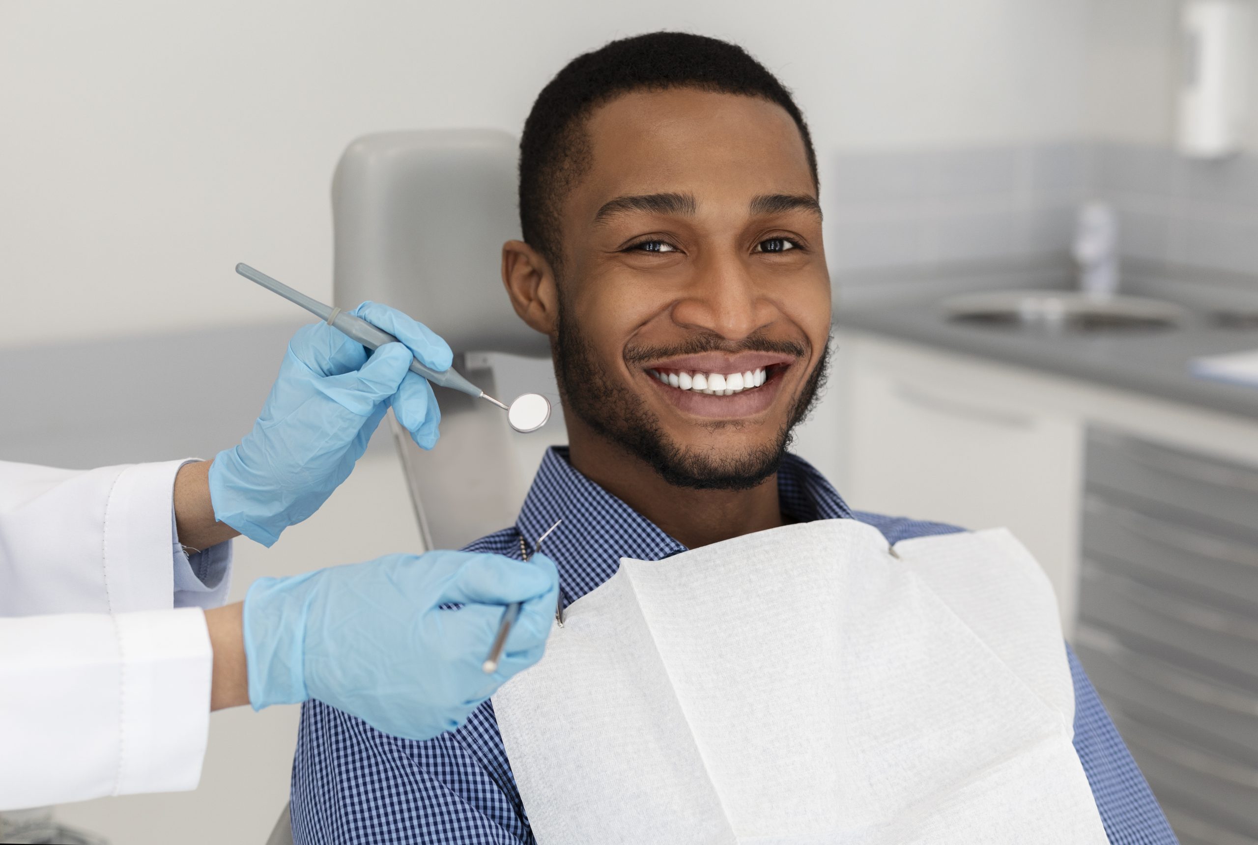 African american man smiling and sitting in dental chair while dentist holds tools
