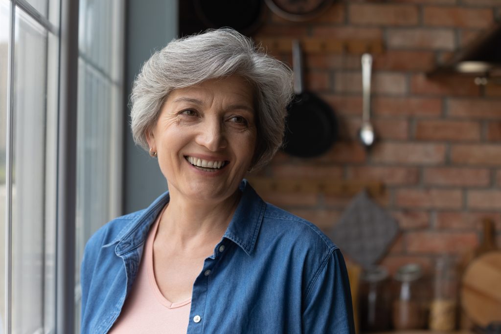 Gray haired elderly woman smiling near window