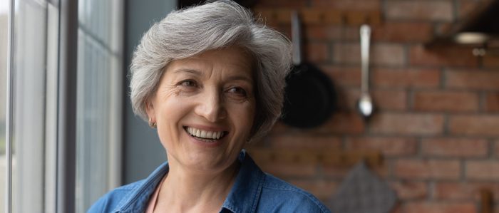 Gray haired elderly woman smiling near window